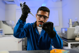 Oscar Molina uses a pipette while wearing protective glasses in a blue-lit lab.