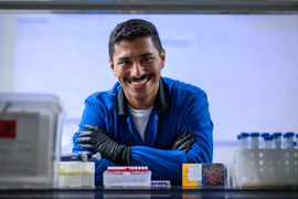 Oscar Molina smiles in the lab while wearing protective jacket and gloves.